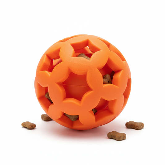 Orange rubber treat dispensing ball toy for dogs with small bone-shaped treats scattered around